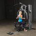 Female athlete seated and performing a row on Body-Solid G5S Home Gym, pulling handles toward her torso.