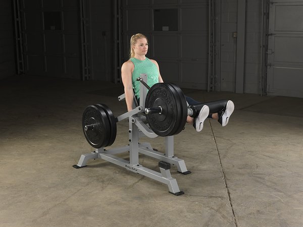 Left side view of female athlete with extended legs on Body-Solid Pro Clubline Leverage Leg Extension LVLE with bumper plates loaded.
