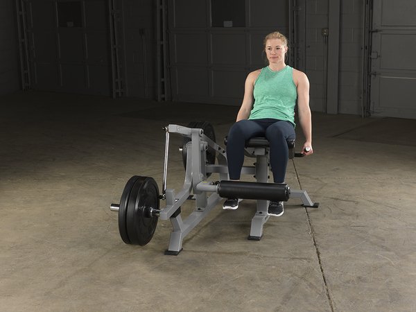 Front view of female athlete in relaxed leg position on Body-Solid Pro Clubline Leverage Leg Extension LVLE with bumper plates loaded.