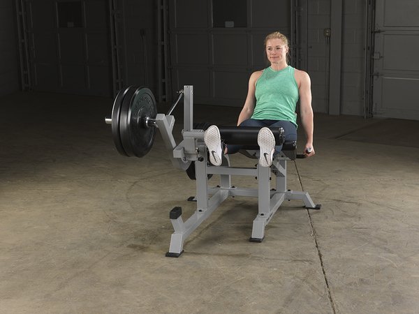 Right side view of female athlete with extended legs on Body-Solid Pro Clubline Leverage Leg Extension LVLE with bumper plates loaded.