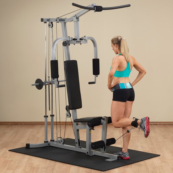 White female athlete in a teal top performing single-leg cable kickback on the Powerline Home Gym PHG1000X.