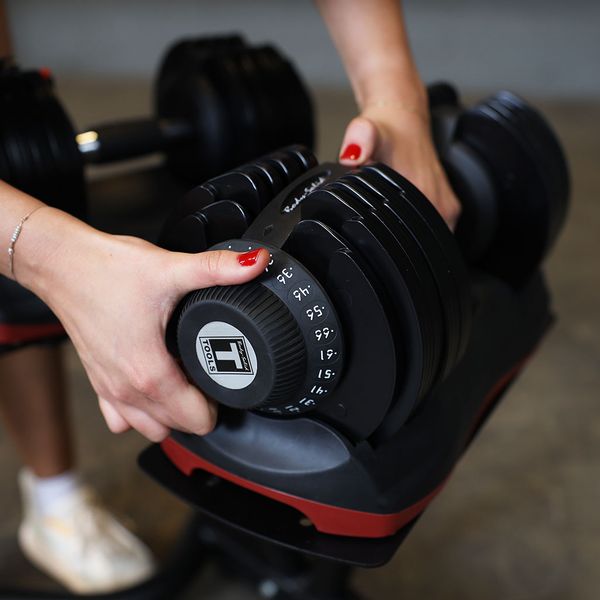 Close-up view of a person adjusting the Dial Tech knob on a Body-Solid Tools SDBX132 Adjustable Dumbbell for selecting weight increments.