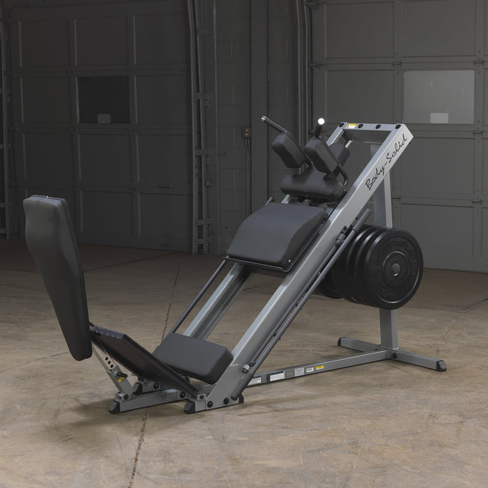 Body Solid Angled Leg Press & Hack Squat Machine side view in a warehouse setting, showcasing the quad track roller system, diamond plate foot platforms, and heavy-duty frame for leg press and hack squat exercises.