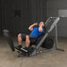 Athlete in starting hack squat position on the Body Solid Angled Leg Press & Hack Squat Machine, feet positioned on diamond plate platform, ready for lower body workout