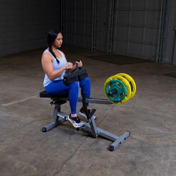Female athlete working out on the Body-Solid GSCR349B Seated Calf Raise Machine with yellow and green weight plates, demonstrating proper use and form.
