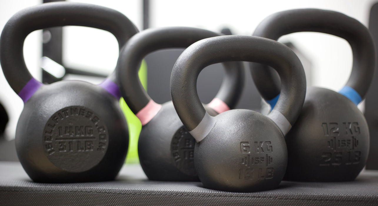Close-up of four ISF kettlebells on a flat weight bench.